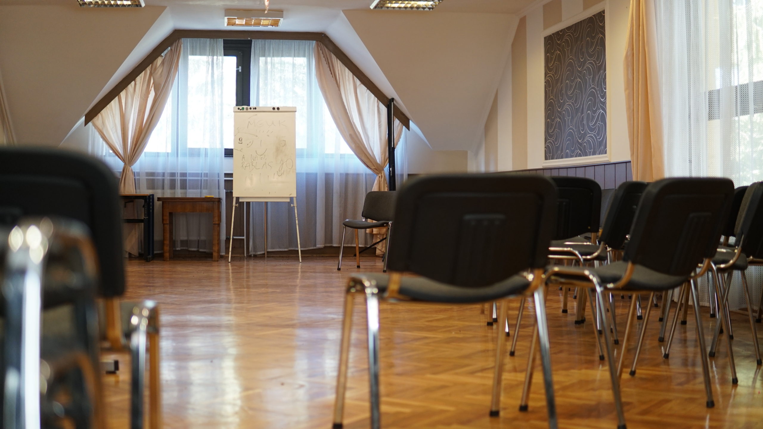 Tárgyalóterem sorokba rendezett székekkel, flipchart-állvánnyal és parkettás padlóval.
